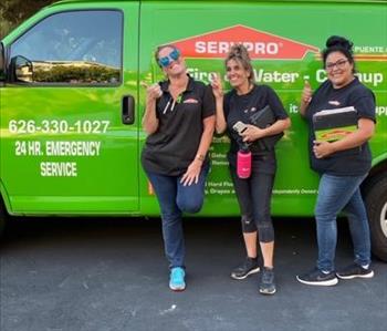 Three women standing in front of a SERVPRO van wearing black SERVPRO shirts and jeans.